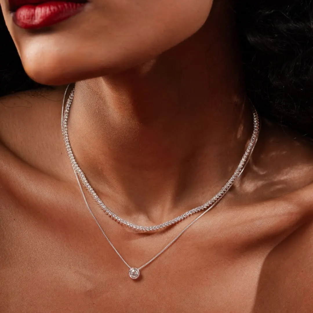 Colo de mulher usando dois colares prateados finos, um deles com pingente ponto de luz.