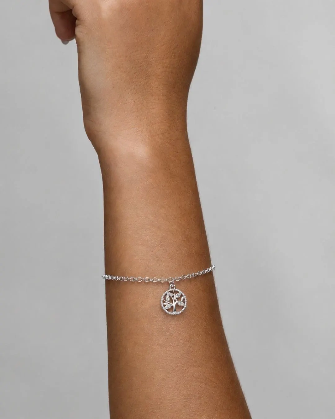 Braço feminino exibindo delicada pulseira prateada com pingente circular de medalha recortada.