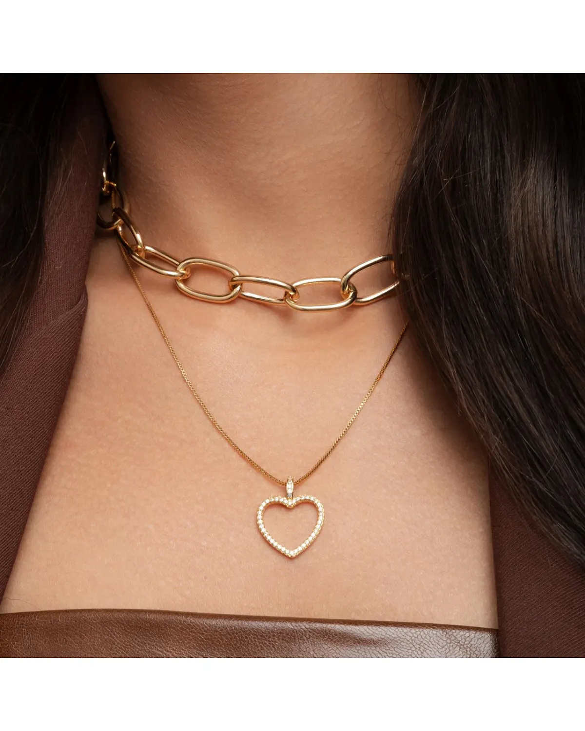 Mulher usando colar choker de elos e gargantilha com pingente de coração vazado dourado.