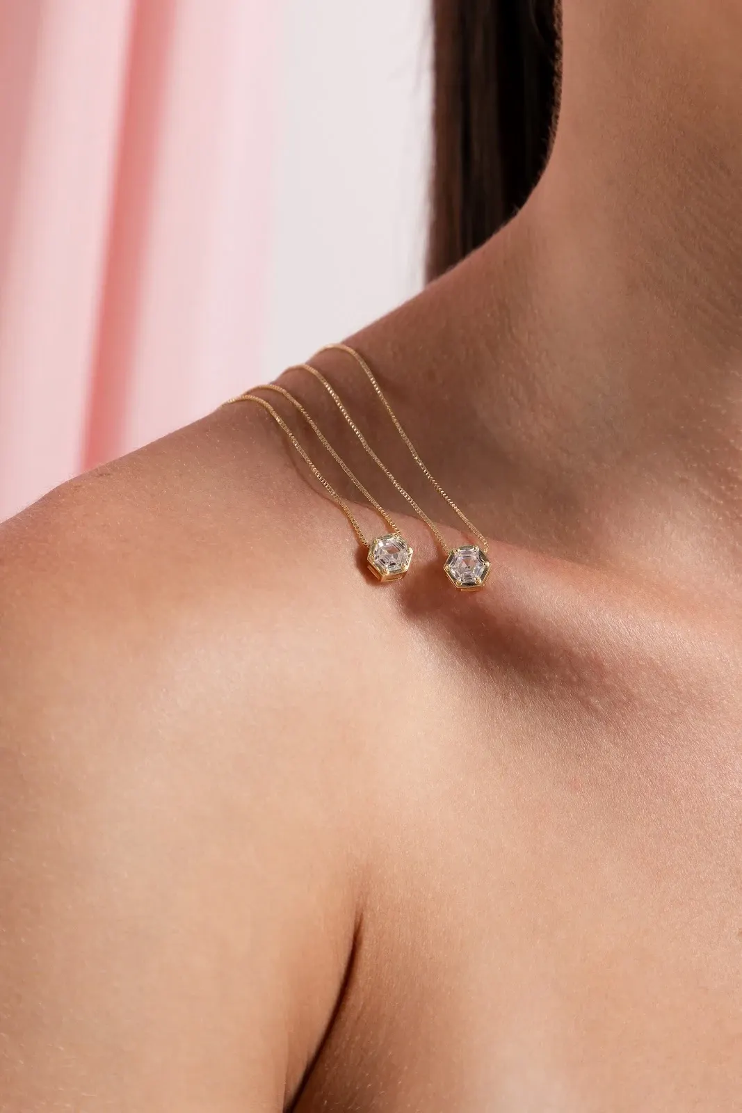 Colares finos dourados com pingentes brilhantes apoiados no ombro de modelo feminina.